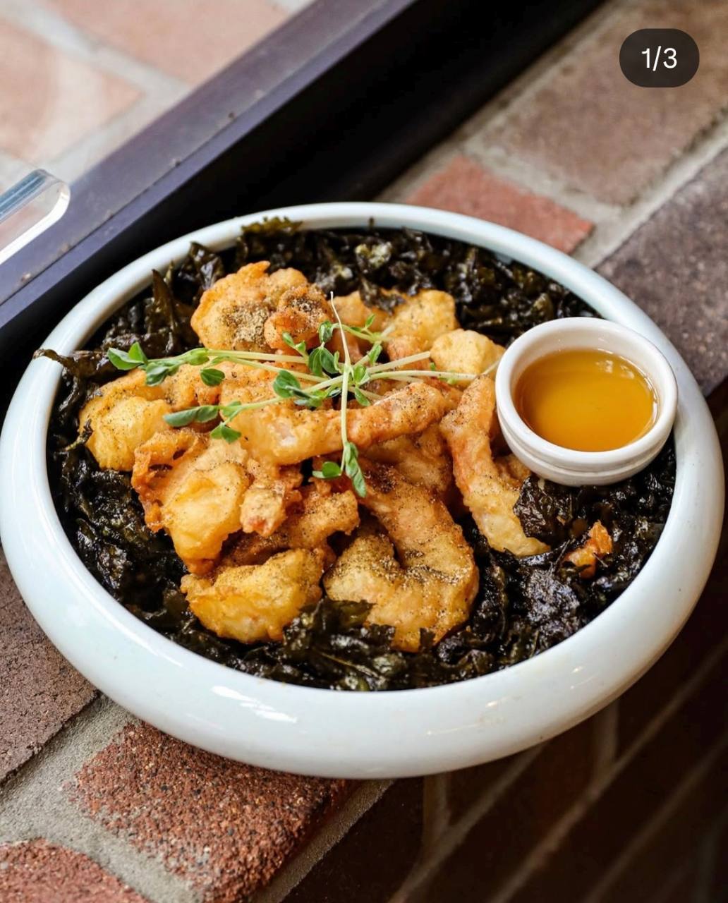 Crispy golden prawns with garnish and dipping sauce in a pale blue bowl